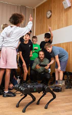 Kinder stellen Moritz Geilinger Fragen zu den mitgebrachten Robotern