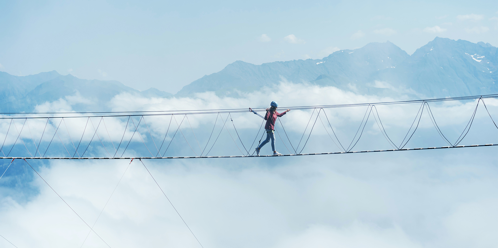 Frau geht auf einer Klettersteigbrücke mit Bergen im Hintergrund