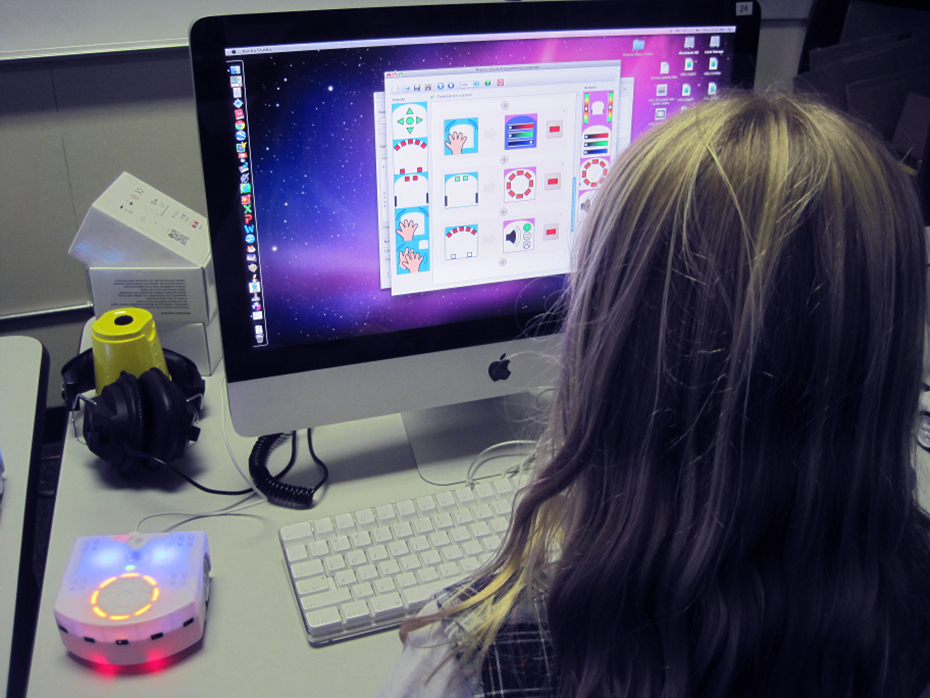 A child uses the visual programming language on a computer to program a Thymio robot.