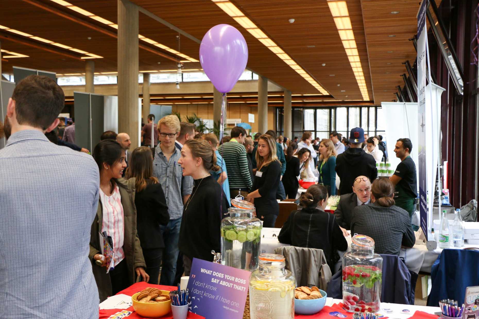 ETH canteen filled with people and exhibition booths, a purple balloon floats above the crowd.