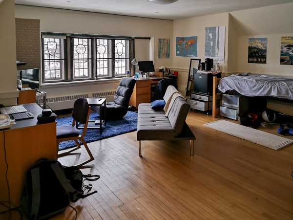 A spacious university dorm room with a wooden floor, a couch, two desks and a bed