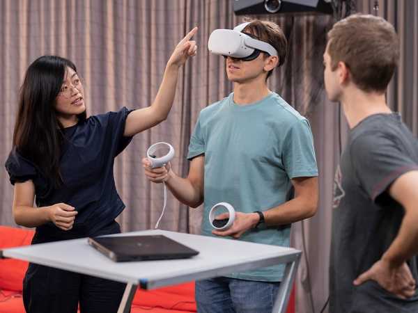 Man with VR glasses and hand controllers, women scientist standing next to him