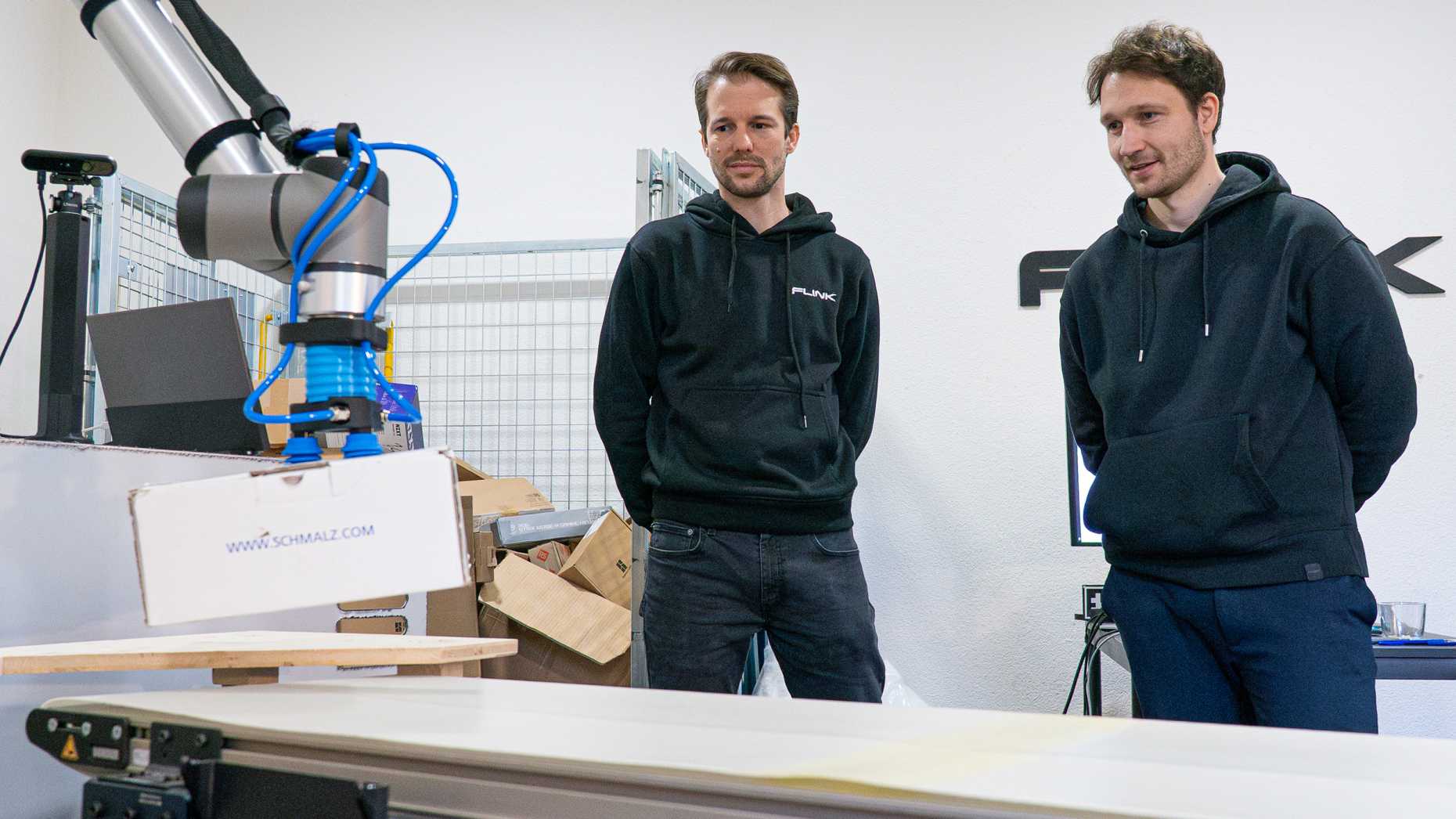 Two men stand in front of a packaging machine.